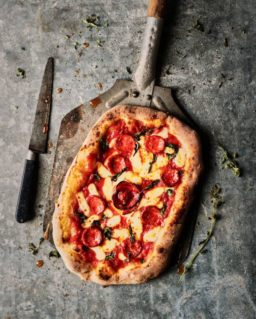 Food and drink photography capturing pizza on paddle straight from oven, real food photography produced in a Sussex studio for editorial and brand use by Rob Morris