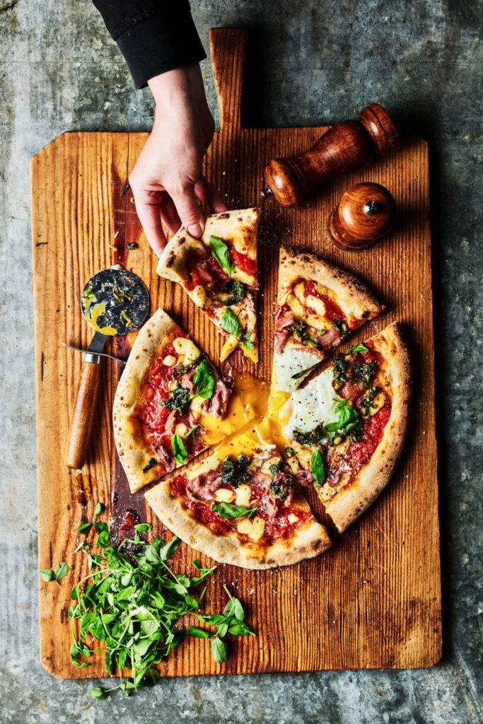 Hand model with pizza, soft egg, rustic food photography, Creative food and drink photography of [dish or drink], styled and photographed in Sussex by a commercial London food photographer