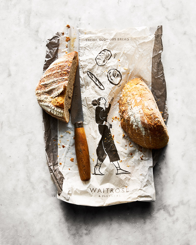 Waitrose rustic bread and bread bag, overhead with bread knife using natural daylight and shot by Rob Morris UK food photographer and food stylist.