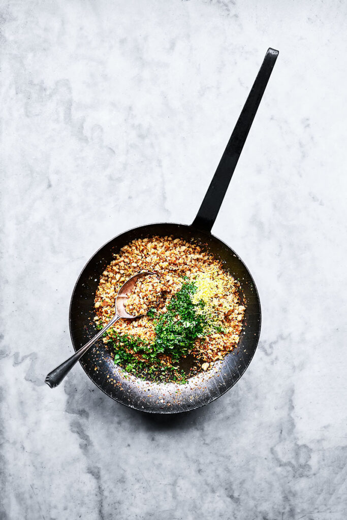 Pangratatto frying pan, overhead with spoon in black pan. Photographed by UK food photographer & Food stylist Rob morris using natural daylight